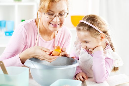 Beautiful happy grandmother and granddaughter broken eggs for the making Dough in a kitchen. 