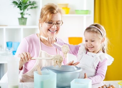 Beautiful happy grandmother learning her granddaughter how to making Dough in the kitchen.