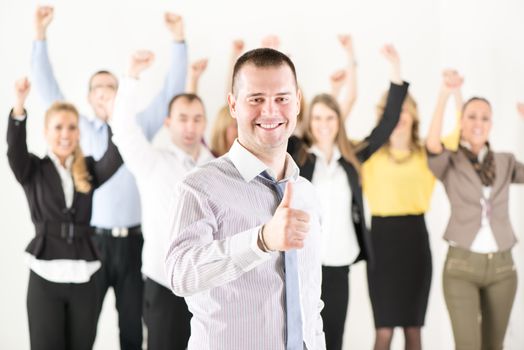 Successful businessman showing Thumbs Up standing in front of happy colleagues and looking at the camera.