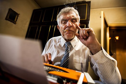 Retro Senior man, journalist, writer, writing on a traditional Typewriter. He is sitting with a cigarette and thinking.