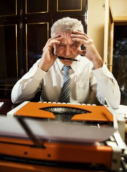 Retro Senior man, journalist, writer, sitting with a traditional Typewriter and thinking, with pen in a mouth.