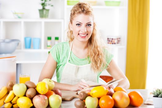 Beautiful young woman reading cookery book in a kitchen. Looking at camera.