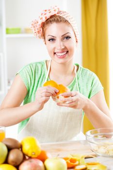 Beautiful young woman peeling oranges in the kitchen. Looking at camera.