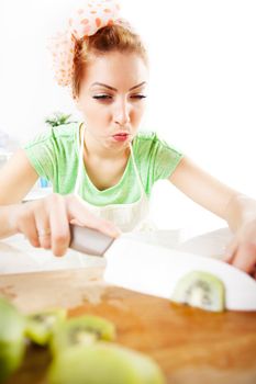 Beautiful young woman cutting kiwi in a kitchen. 