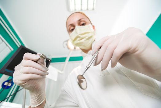 Dentist holding dental drill and Angled Mirror for inspecting a patient. Selective Focus.