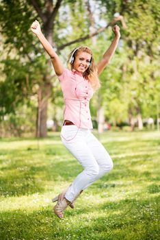 Happy young woman with headphones jumping in park and having fun.