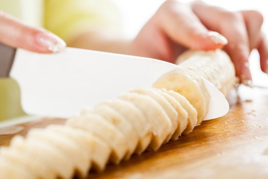 Female hands Cutting Banana on the kitchen board. Close-up. Selective Focus.