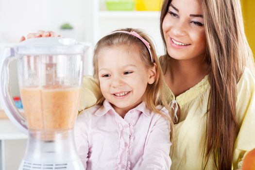 Beautiful young woman and cute little girl preparing healthy drink / meal in a blender in the kitchen.