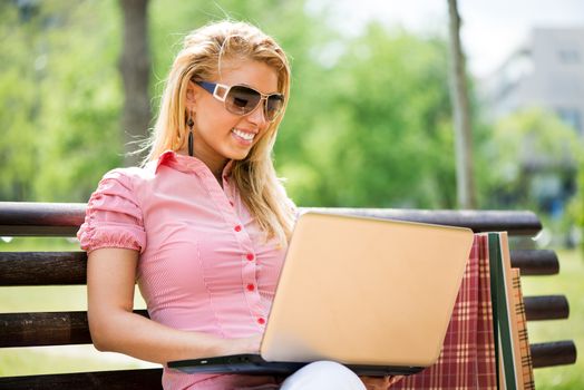 Young Beautiful Woman sitting and relaxing on the Park Bench and using laptop.