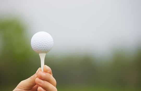 Human hand holding golf ball on a support
