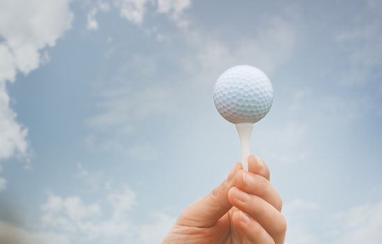 Human hand holding galf ball against the sky background