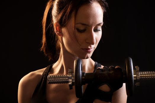 Portrait of a beautiful woman exercising with dumbbells on black background.