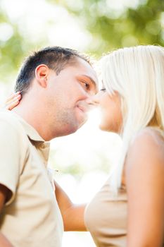 Beautiful embraced romantic couple in the park kissing each other in the front of sunlight.