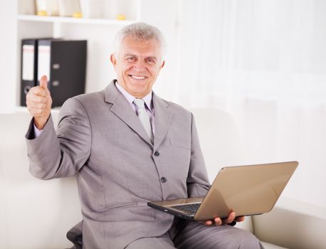 Happy Senior businessman working on laptop and showing thumbs up.