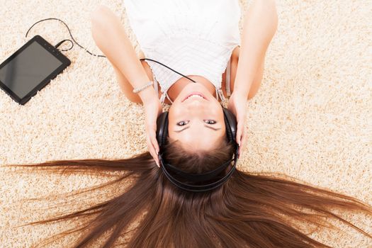 Beautiful young girl lying on the floor and listening music.