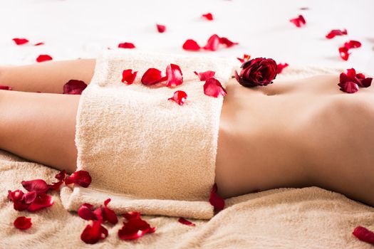 Beautiful female body covered with a towel and petals of roses.