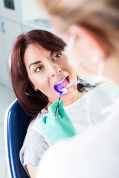 Dentist with dental curing UV lamp finishing repair tooth on the female patient in the office. Selective focus, focus on the patient.