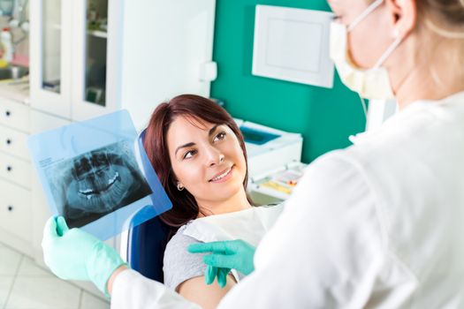 Young female dentist showing to the patient X-ray picture in she`s office.