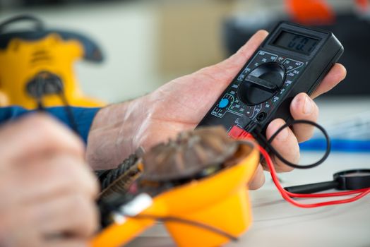 Electrician using Digital Voltmeter for Testing Voltage on old hair dryer. Close Up. Selective focus.