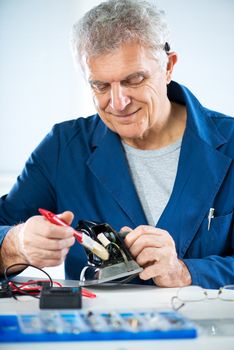 Senior adult Electrician cleaning old iron with soft brush, before repairing.