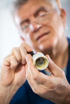 Senior adult Repairman examining and fixing old ceramic bulb socket. Close-up. Selective focus, Focus on socket.