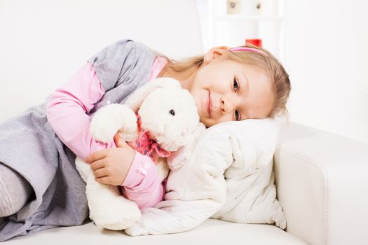 Cute little girl hugging soft toy on sofa at home.