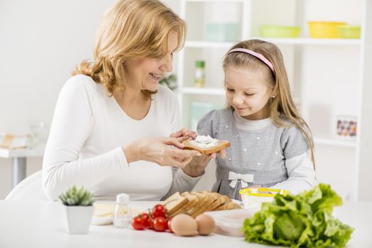 Cute little girl with Grandmother making a Sandwich in the kitchen.