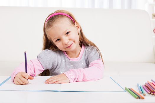 Cute little girl drawing with colored pencils at home.