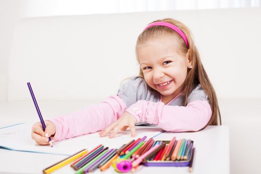 Cute little girl drawing with colored pencils at home.