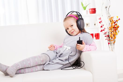 Cute little girl listening music with headphones at home.