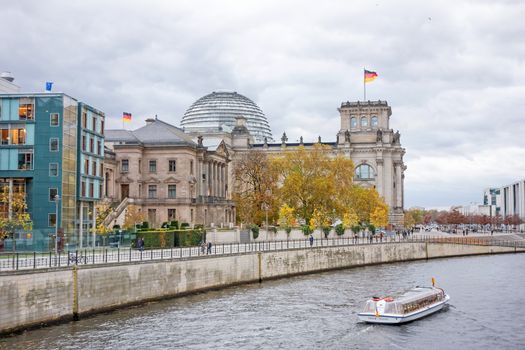 Berlin, Germany - October 28, 2013: Spree river with sightseeing passenger boat and Reichstag building in the background. Government district in Berlin-Mitte, where politic is made in Germany.