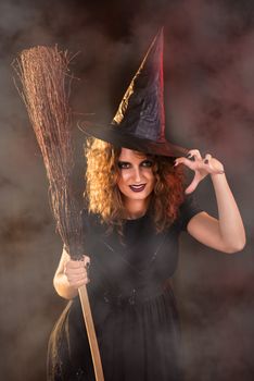 Young woman dressed like a witch. She is in dark clothing and holding a broom.