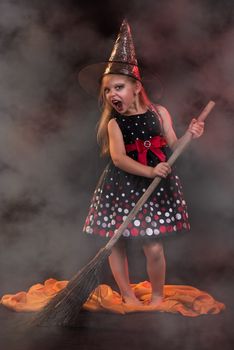 Little halloween witch in dark clothing with broom.