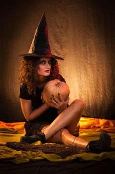 Young woman dressed like a witch. She was wearing dark clothing with a pumpkin in her hands.