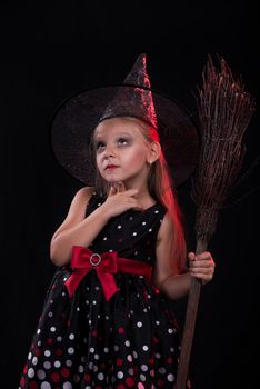 Little girl in dark clothing with broom on black background. She thinks.