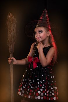 Little girl in dark clothing with broom on black background. She thinks.