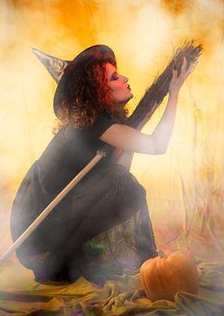 Young woman dressed like a witch. She is in dark clothing with broom.