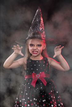 Little halloween witch in dark clothing with evil face.