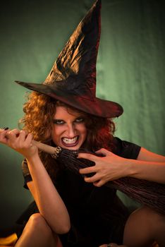 Young woman dressed like a witch. She is in dark clothing with broom.