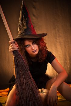 Young woman dressed like a witch. She is in dark clothing with broom.