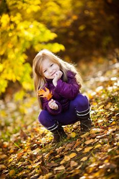 Cute Little girl in the park crouching with yellow leaf
