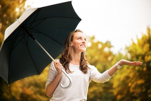Young beautiful woman standing in a rainy autumn park with umbrella.