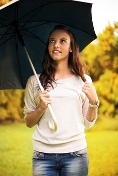 Young beautiful woman walking in rainy autumn park with umbrella.