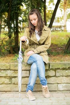 Lonely sad woman sitting on the stone wall in the park.