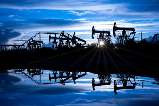 Oil pump jacks group on a sunset sky background. Toned blue.
