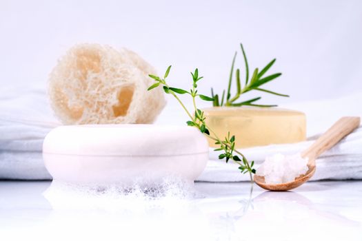 Herbal spa soap bar on white bath towel with thyme,rosemary and luffa isolated on white background.