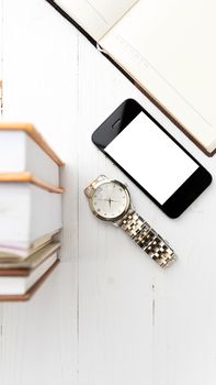 cellphone with stack of book and watch over white table