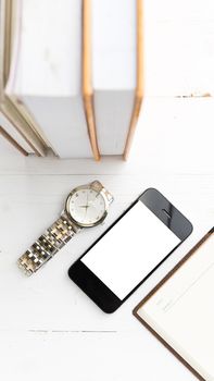 cellphone with stack of book and watch over white table