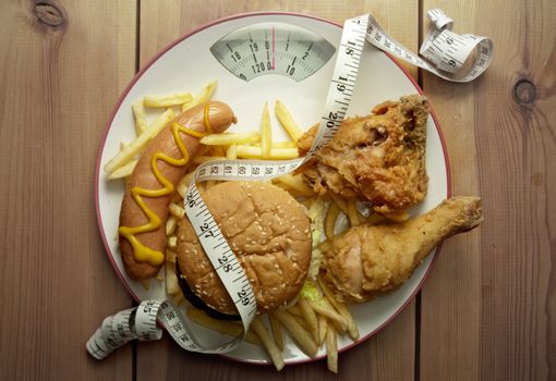 Plate packed with junk food with weighing scales 