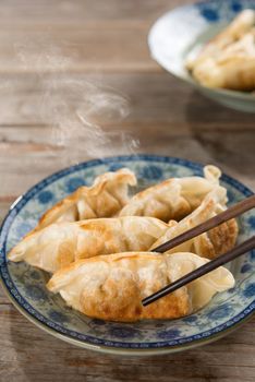Fresh pan fried dumpling on plate with chopsticks. Chinese food with hot steams on rustic vintage wooden background. Fractal on the plate is generic print.